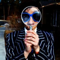 Person holding magnifying glass, photo by Mar Newhall