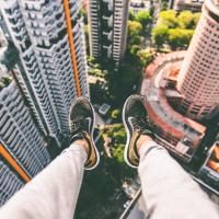 A person's legs dangling off the edge of a building, photo by Alex Wong