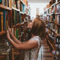 Woman looking for a book in the shelves of a library, photo by Clay Banks