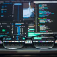 A pair of eyeglasses in front of a computer with code on the screen