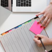 Project manager writing on a sticky note next to a planner and laptop