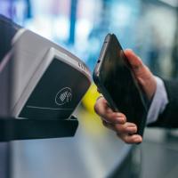 Person making a mobile payment using contactless card technology by waving an Android phone in front of an NFC reader