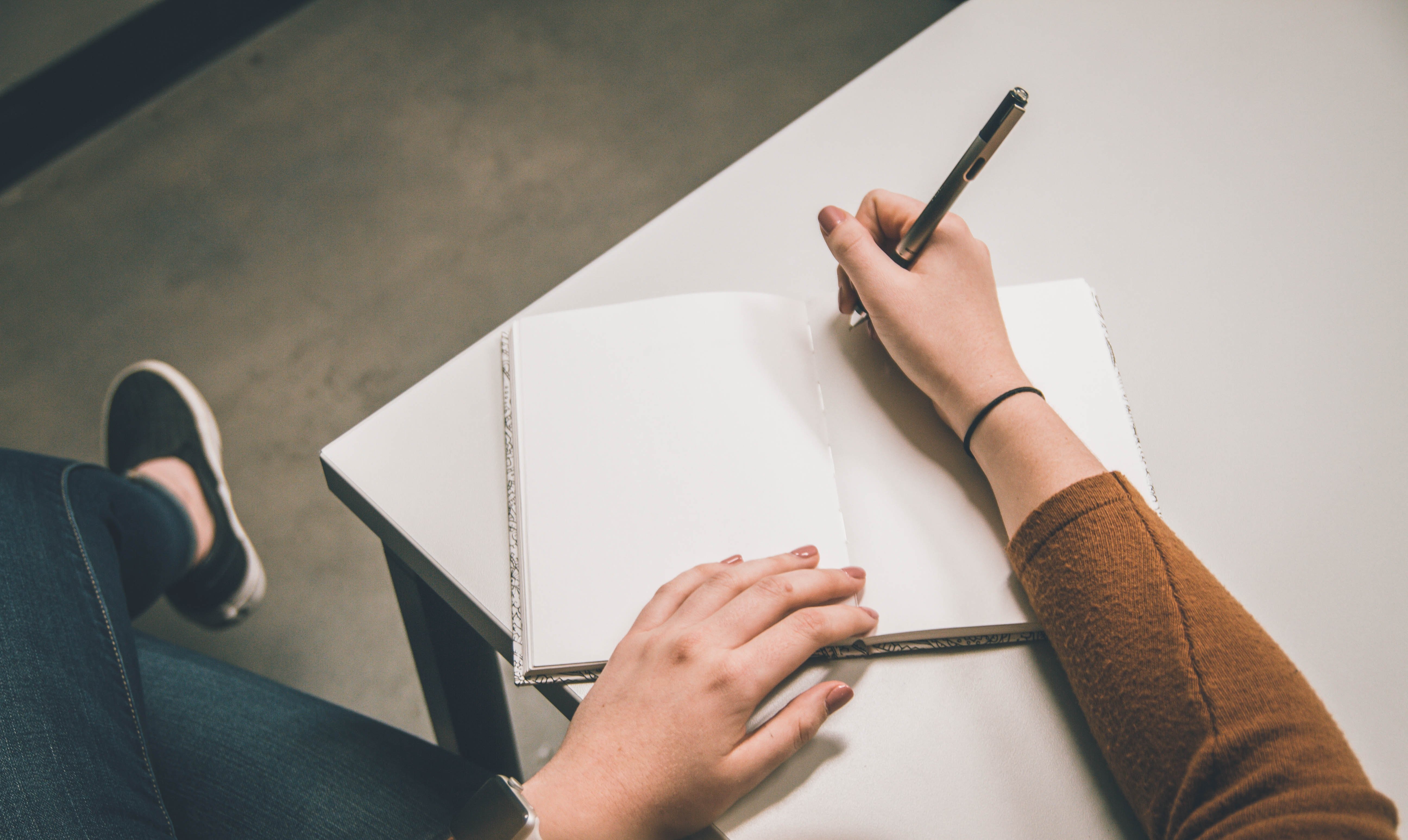 Person with writer's block holding a pen over a blank piece of paper