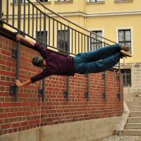 An agile acrobat holds himself perpendicular to a wall