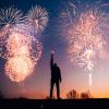 Person holding a sparkler with New Year's fireworks in the background