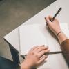 Person with writer's block holding a pen over a blank piece of paper